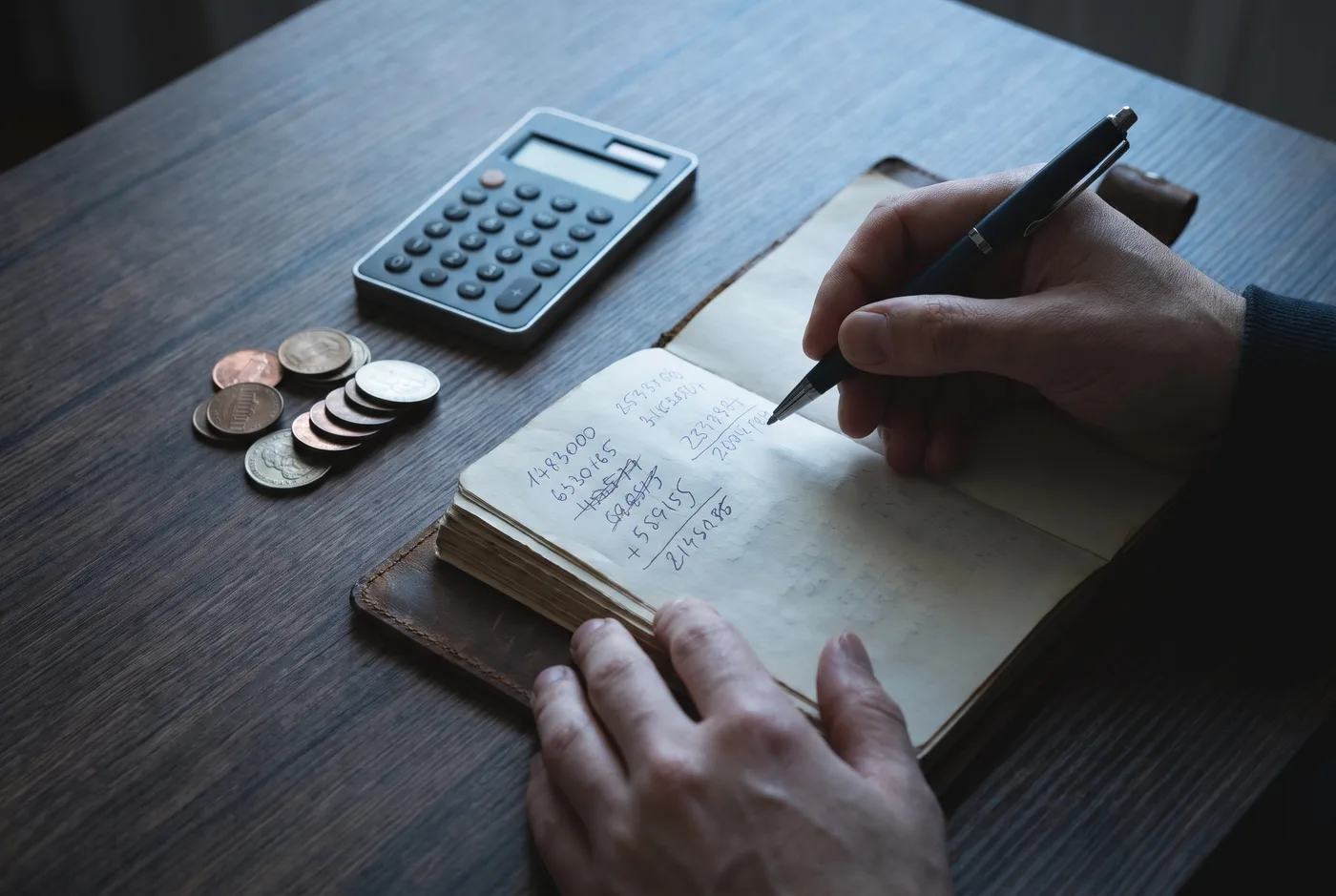 Handen met rekenmachine en notitieboek bij het berekenen van een maandbudget